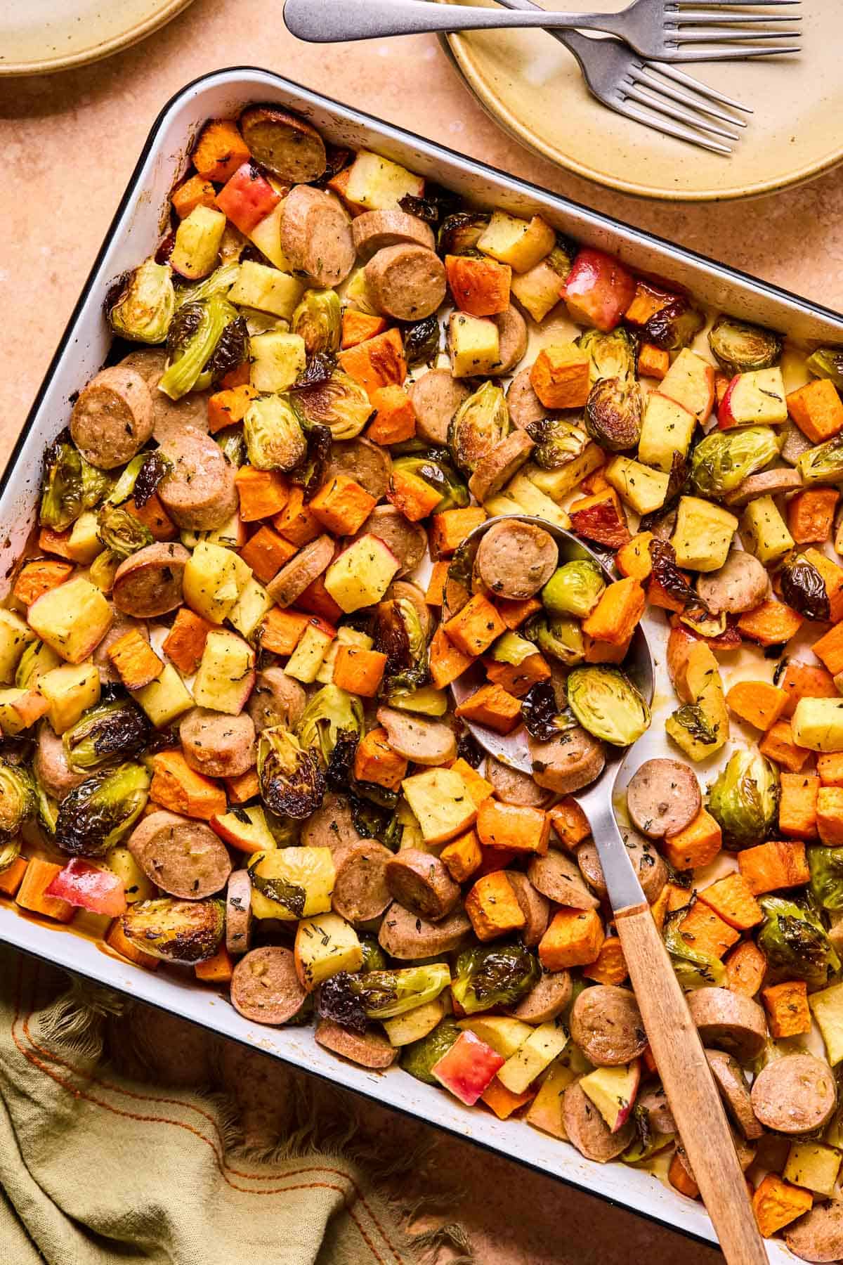 sheet pan full of maple dijon sausage and veggies with a spoon scooping.