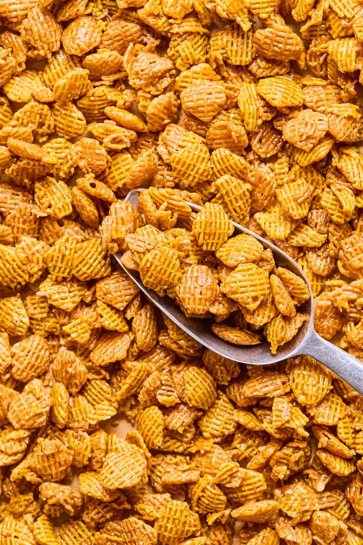metal scoop scooping up salted caramel crispix mix off of a sheet pan