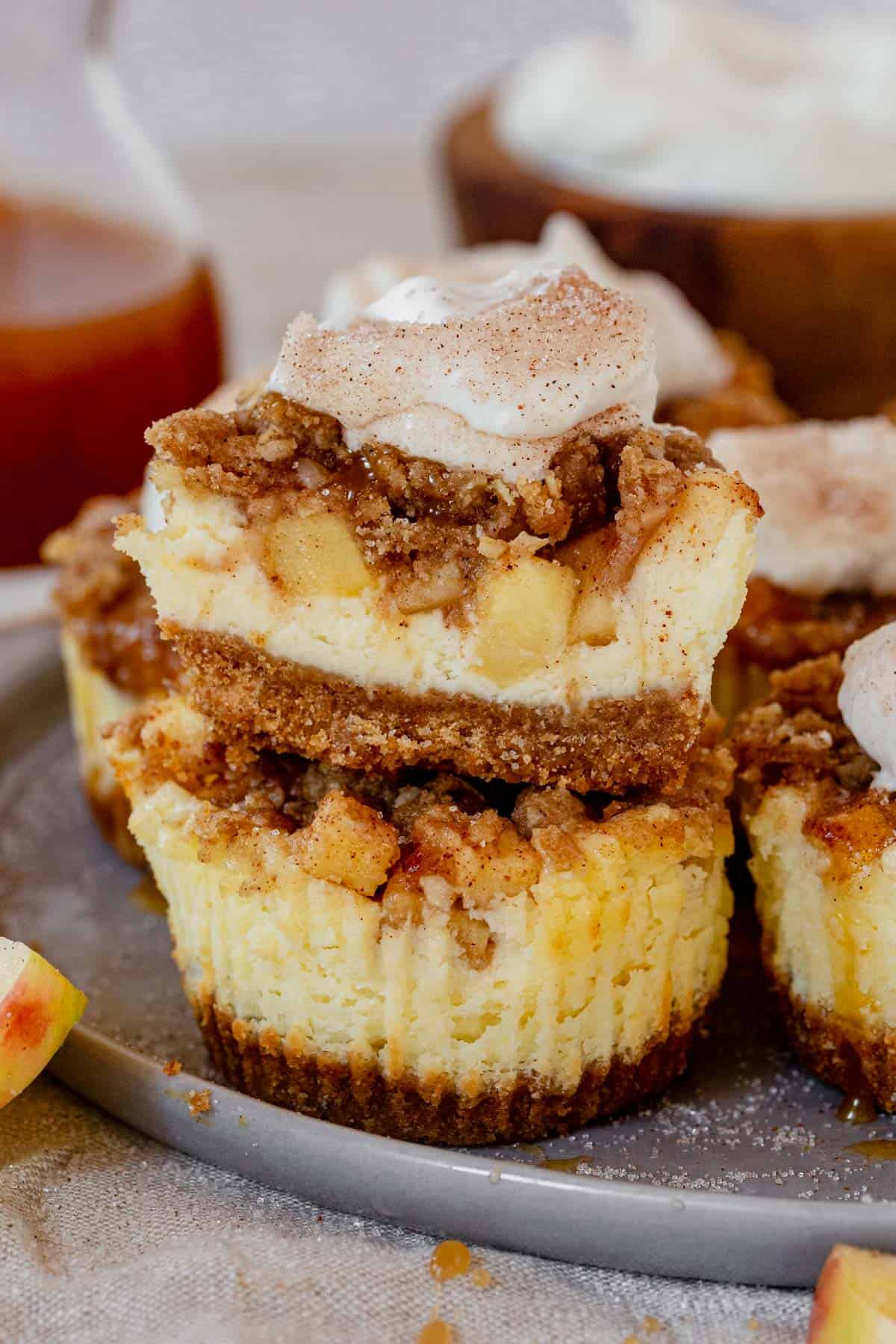 two apple crisp mini cheesecakes stacked on a plate with a bite missing from the top one.