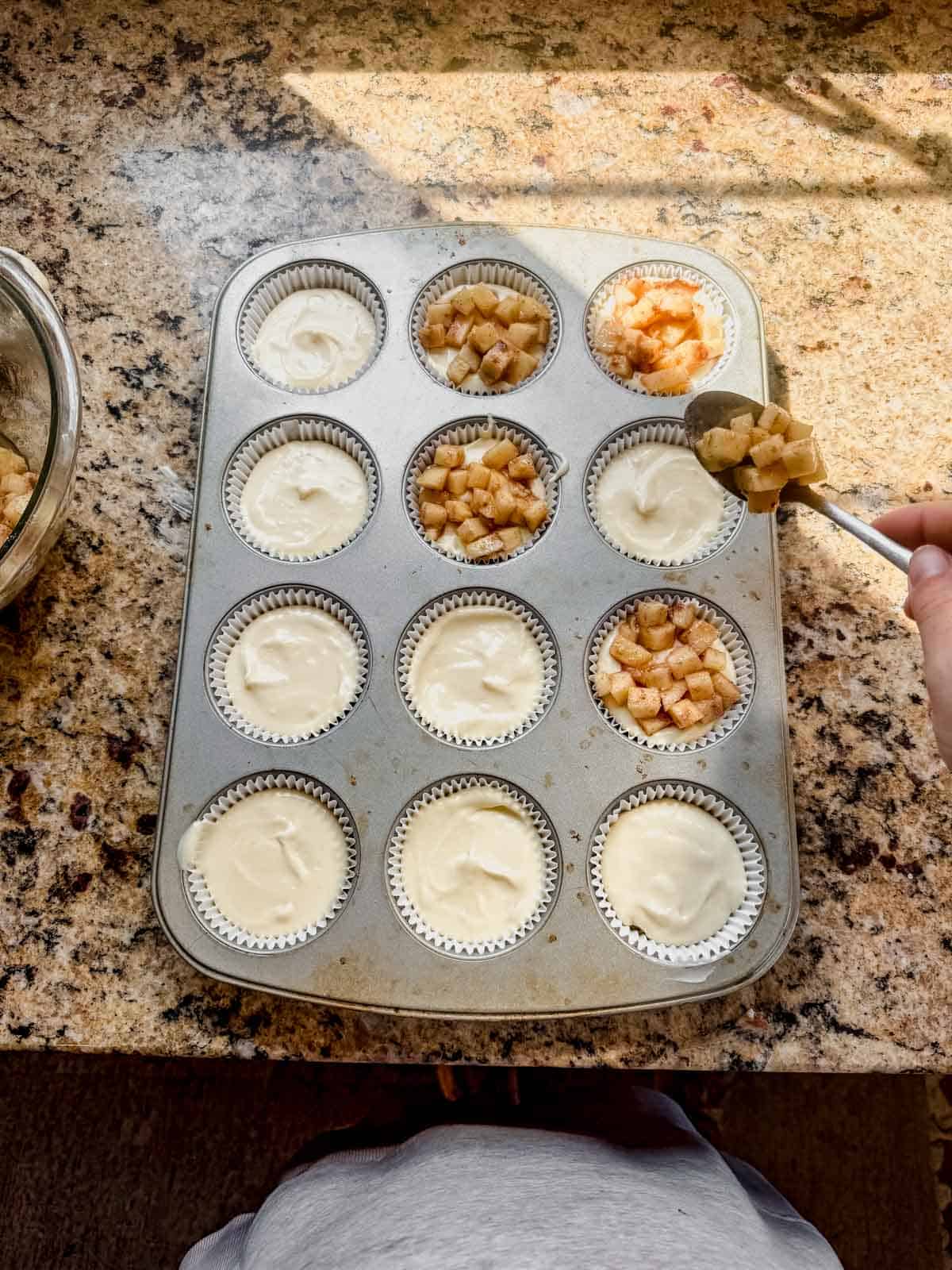 layering apple filling on top of cheesecake and graham cracker crust in mini muffin tins.