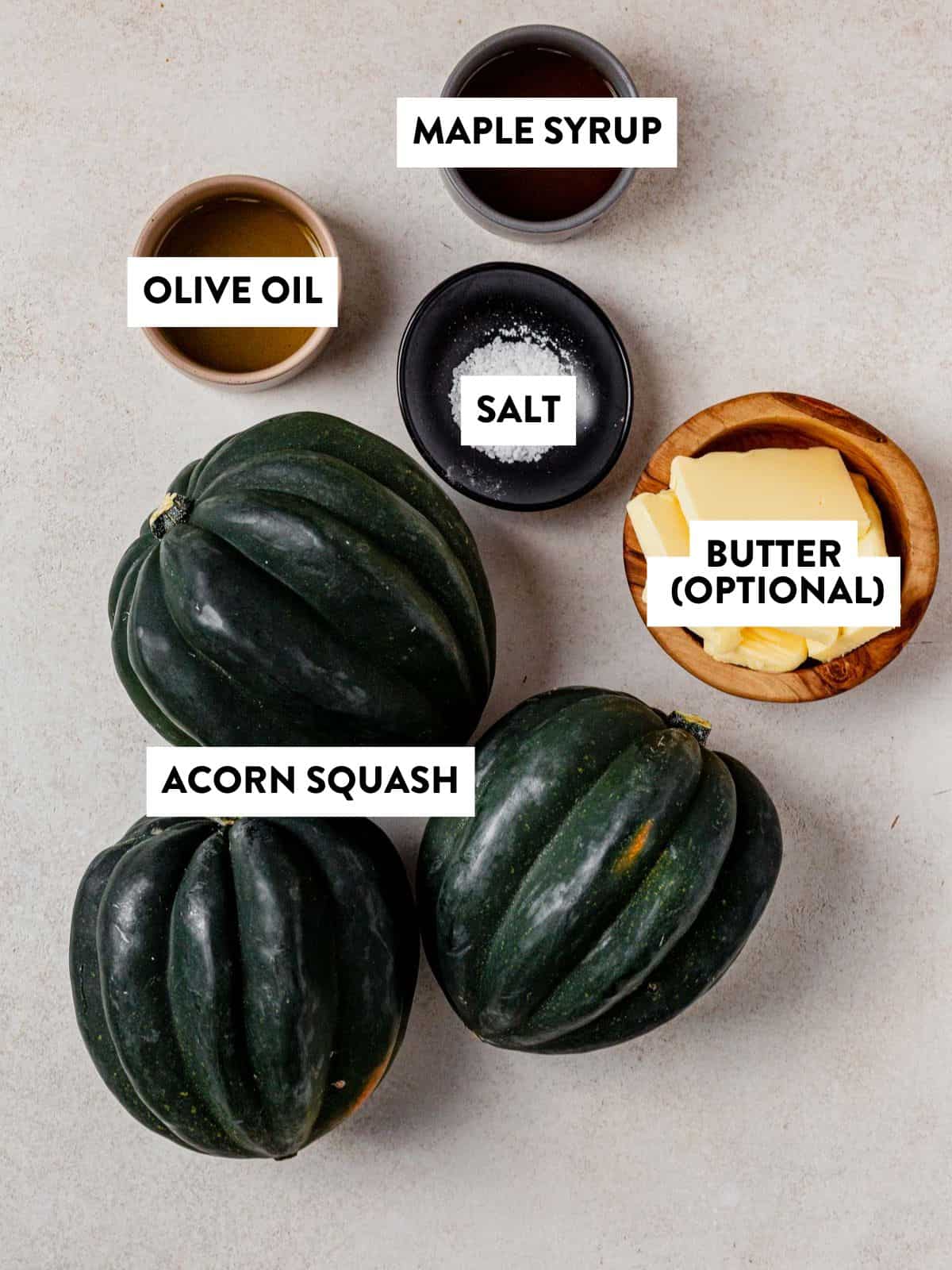 acorn squash, butter, salt, olive oil, and maple syrup on a counter.
