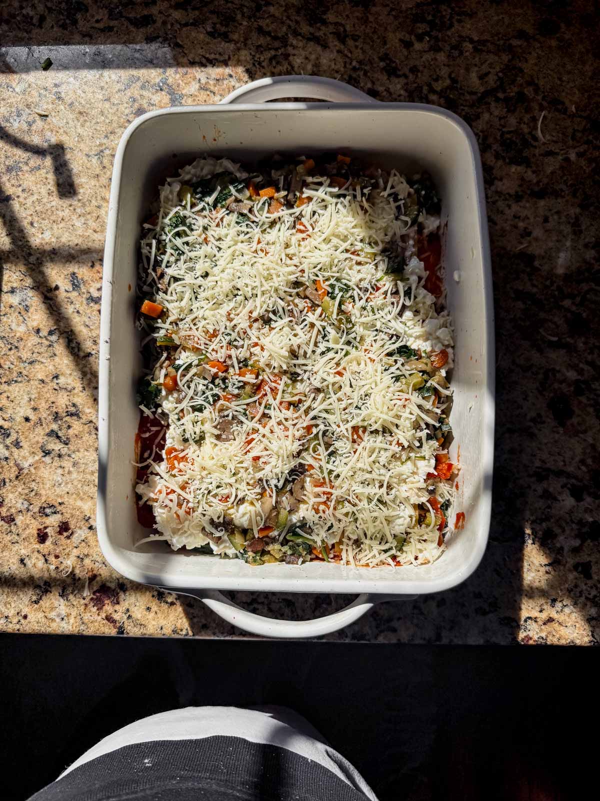 layering cottage cheese vegetable lasagna into a casserole dish.