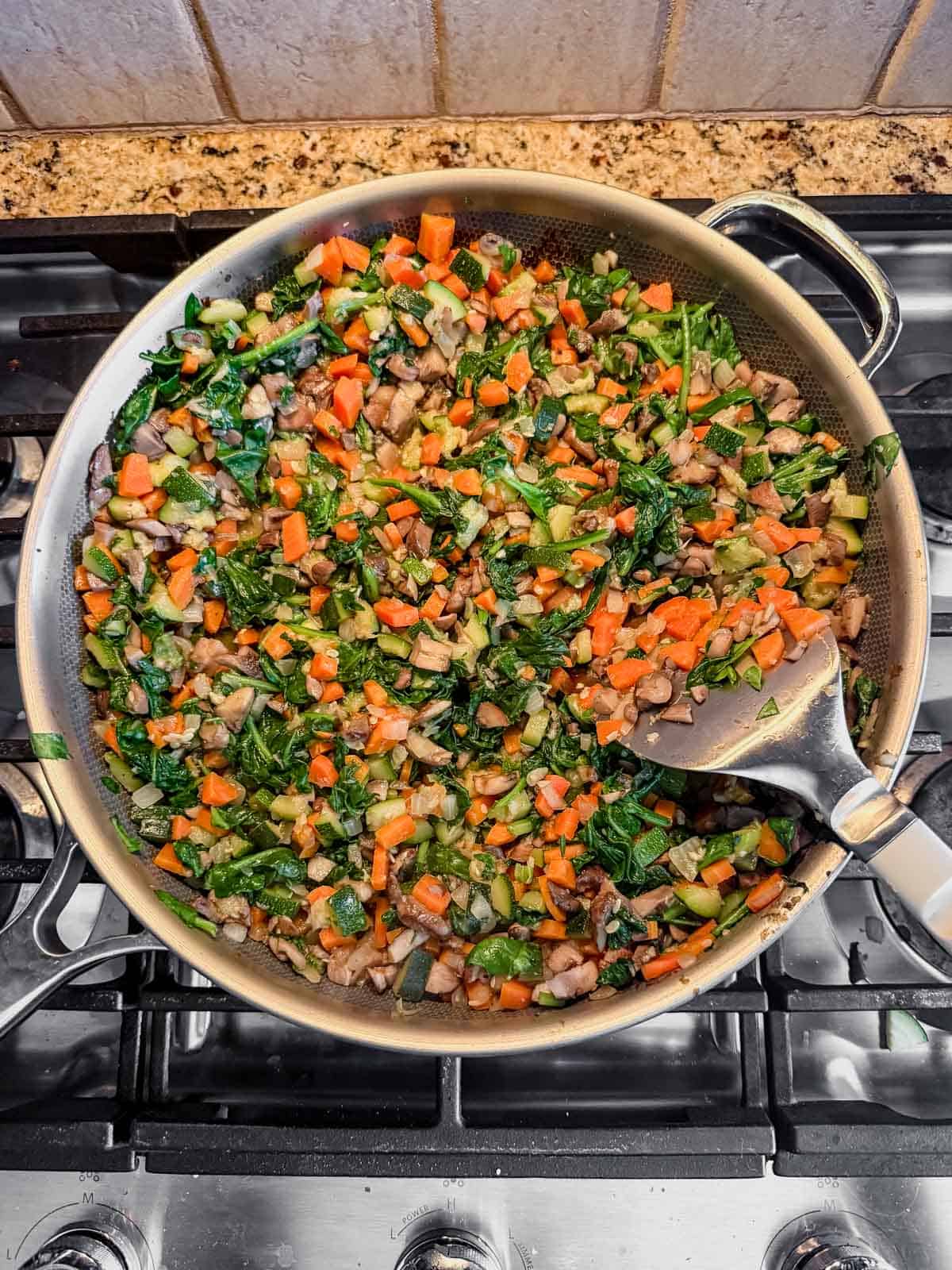 cooked diced vegetables and wilted cooked spinach in a skillet on the stove.