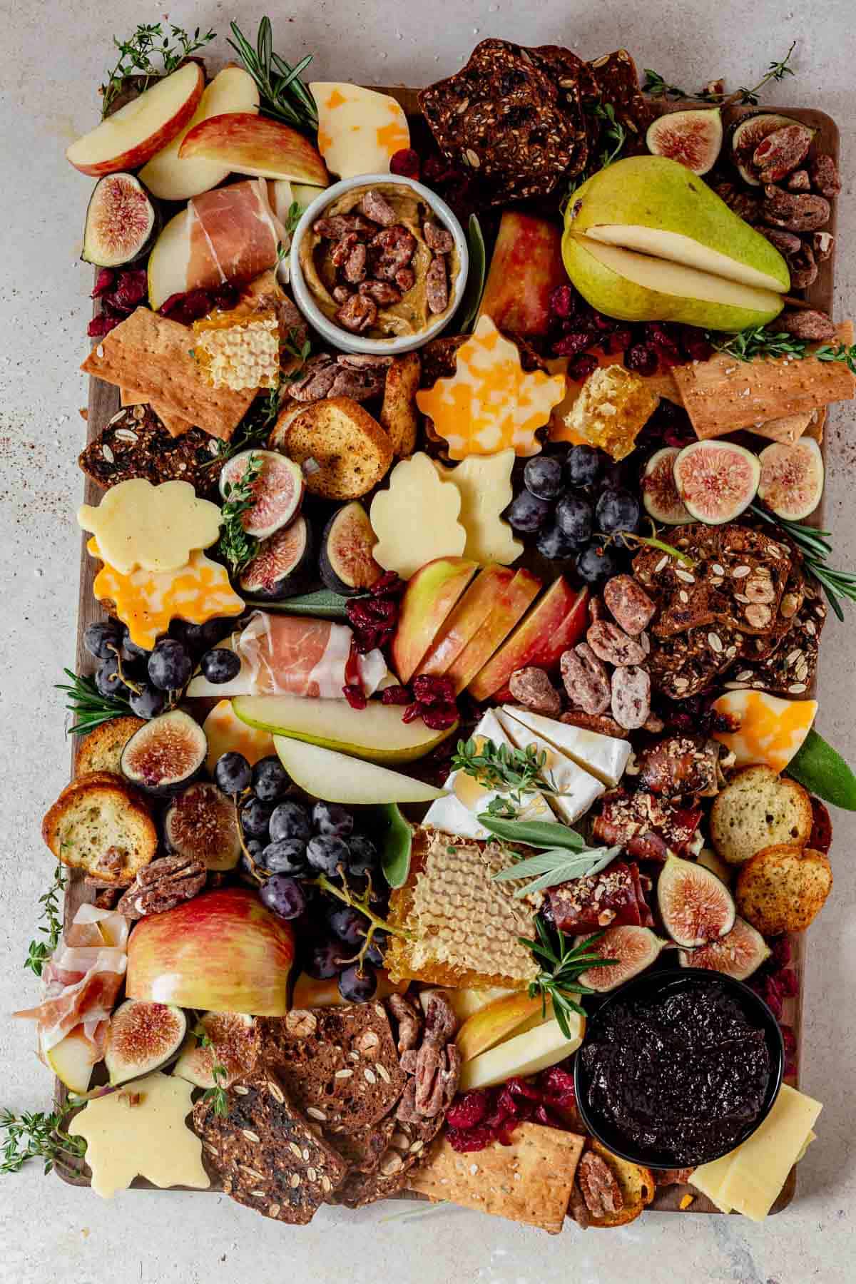 a fall charcuterie board on with pears, apples, candied nuts, fig jam, honey, meat, and cheese.