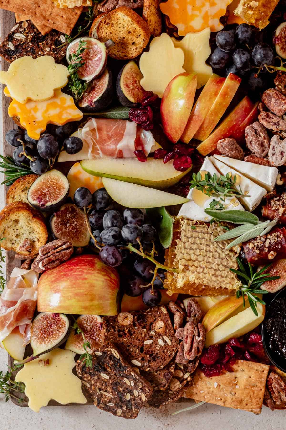 crackers, honeycomb, leaf shaped cheese, and figs on a cutting board.