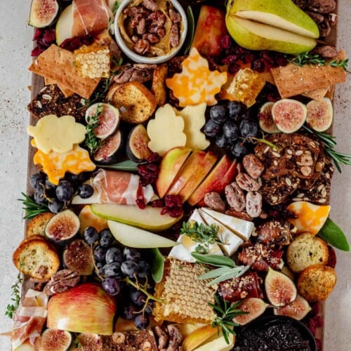 a fall charcuterie board on a counter with leaf shaped cheese, honey, pear, apples, candied pecans, and crackers.