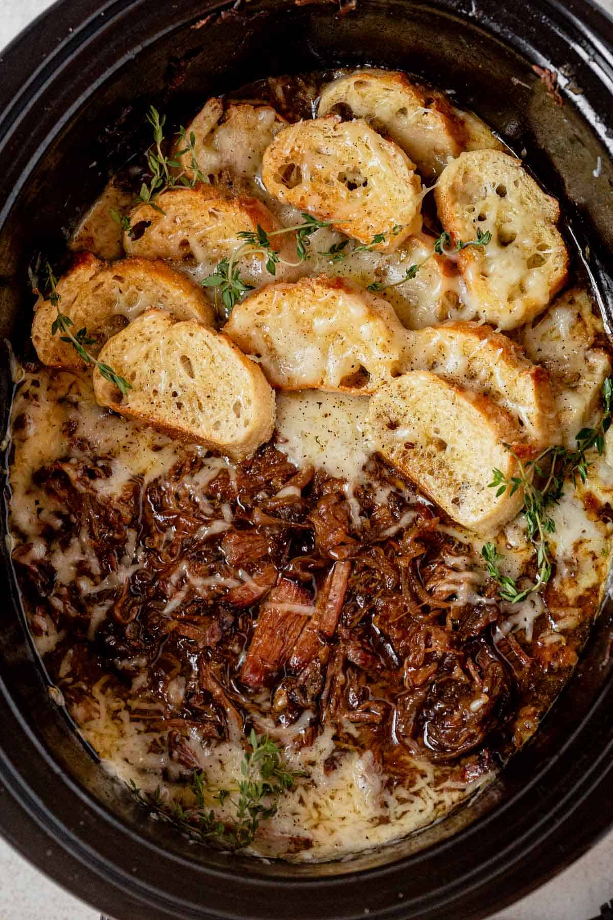 french onion pot roast in the slow cooker topped with french bread and melted cheese.