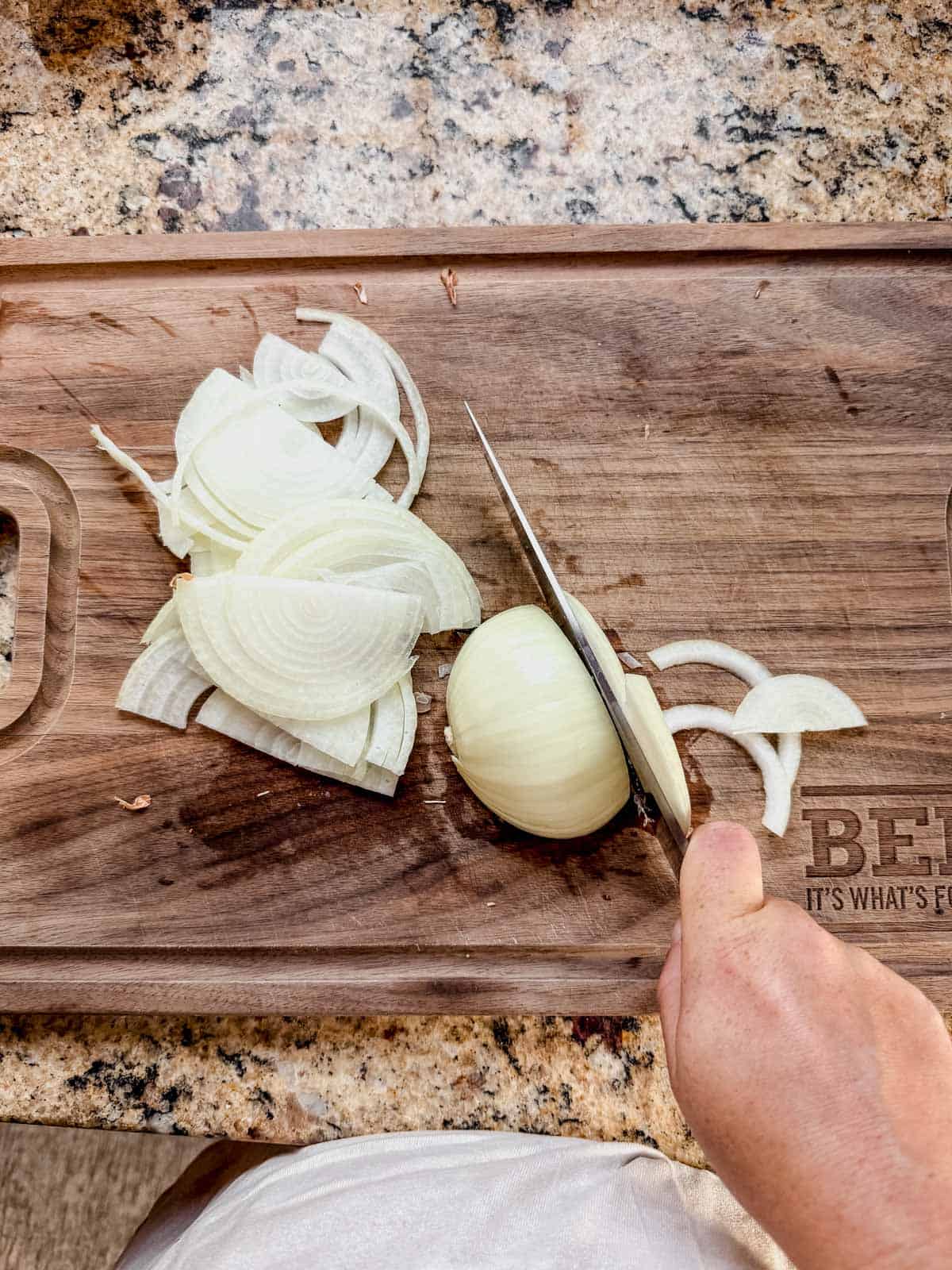 thinly slicing an onion on a cutting board for french onion pot roast.