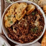 a bowl of french onion pot roast with toasted bread, cheese, and thyme.