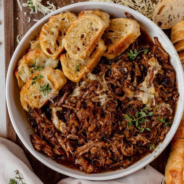a bowl of french onion pot roast with toasted bread, cheese, and thyme.
