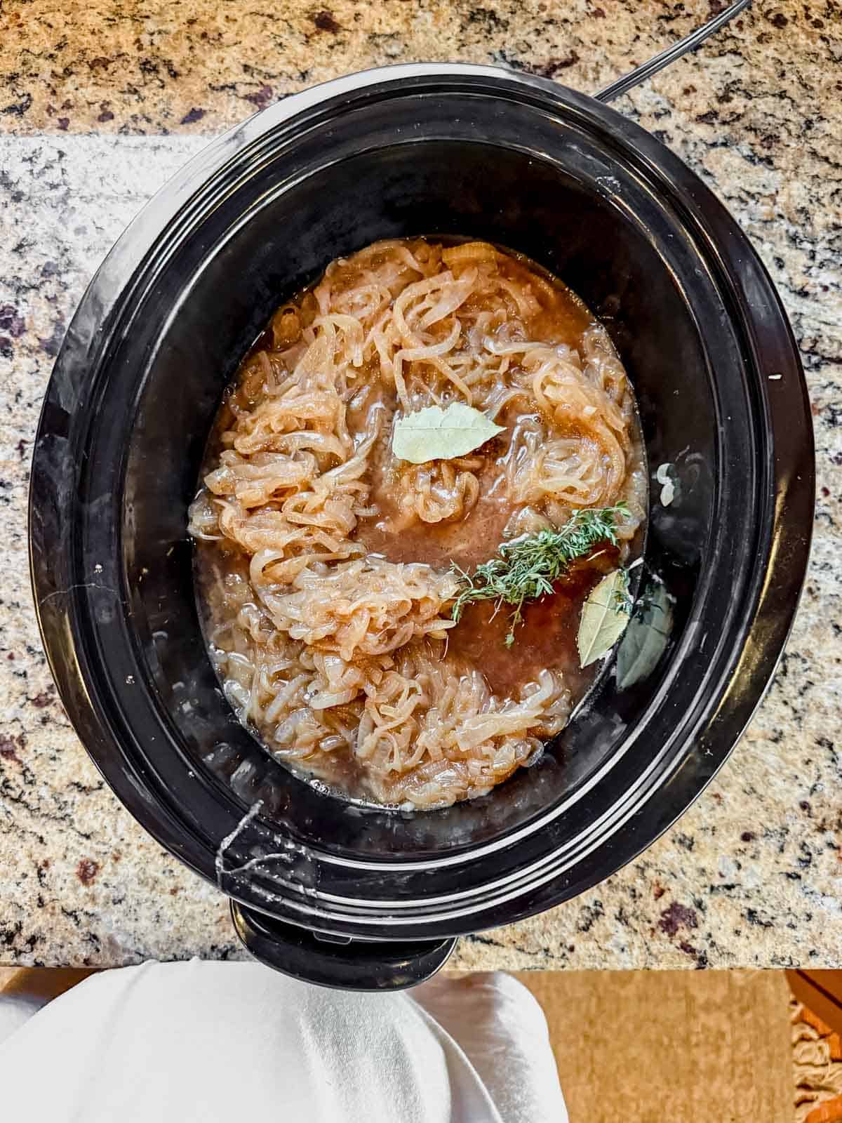 chuck roast, caramelized onion, and herbs in a crock pot before slow cooking.
