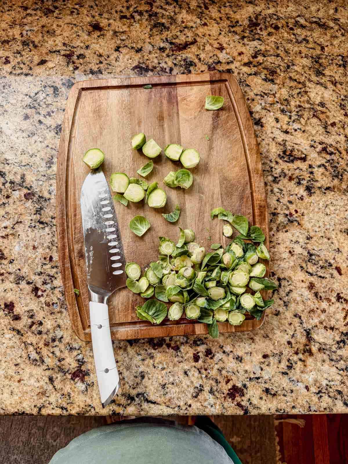 trimmed and halved brussels sprouts on a wood cutting board.