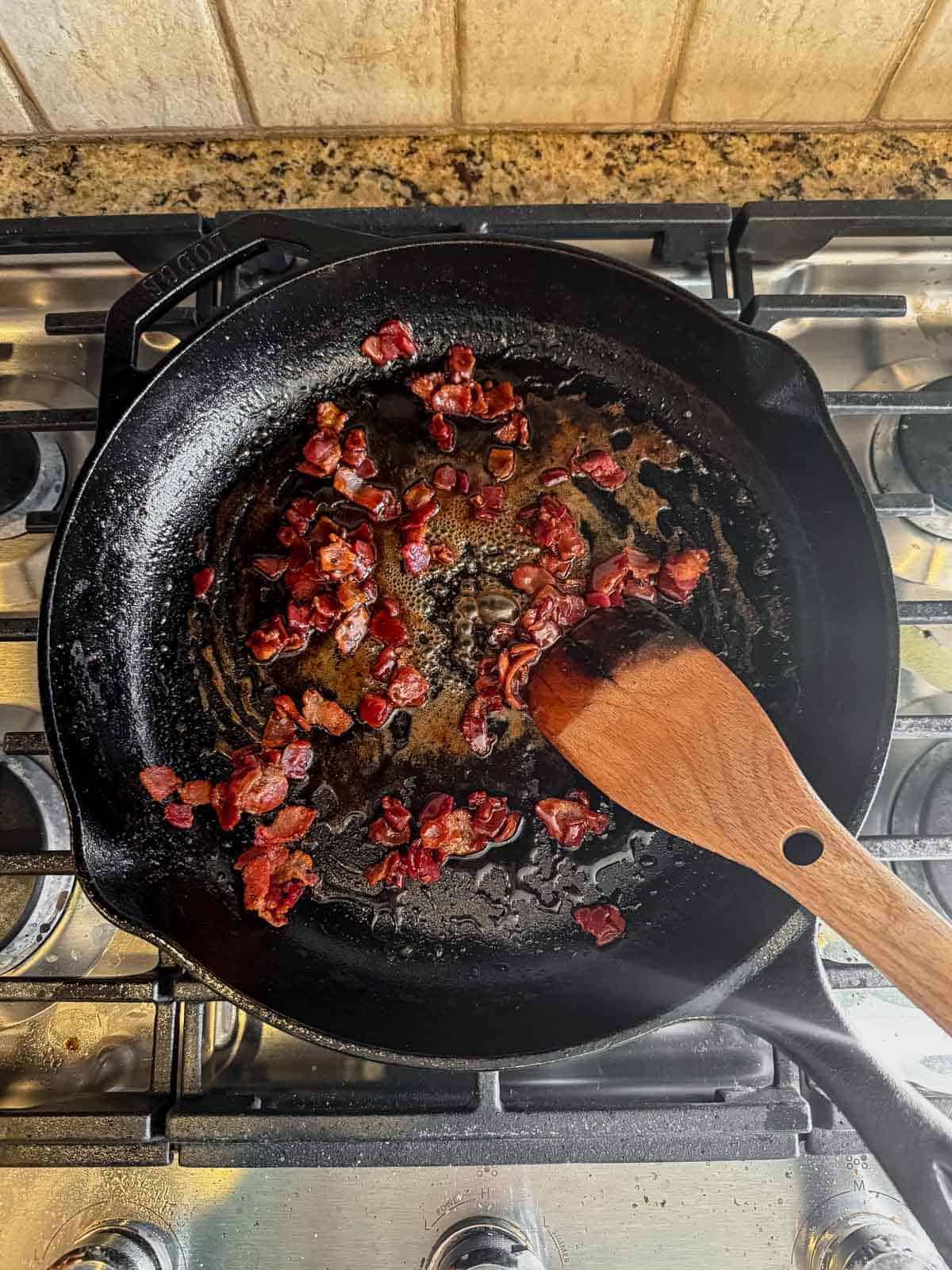 cooking crispy bacon bits in a cast iron skillet.