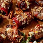 crisp prosciutto wrapped dates on a serving platter with pecans and honey on top.