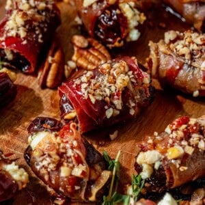 crisp prosciutto wrapped dates on a serving platter with pecans and honey on top.