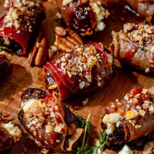 crisp prosciutto wrapped dates on a serving platter with pecans and honey on top.