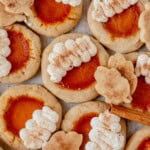 pumpkin pie cookies on parchment paper decorated with whipped cream and cinnamon sugar.