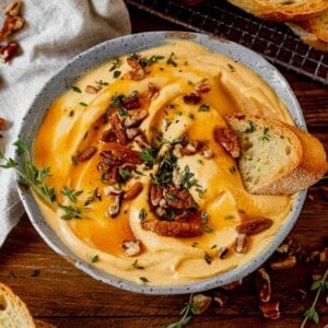 creamy pumpkin whipped feta dip in a bowl topped with honey and pecans and a piece of bread in it.
