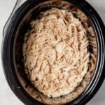 juicy shredded chicken in the slow cooker with salt and pepper on top.