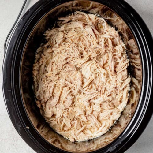 juicy shredded chicken in the slow cooker with salt and pepper on top.