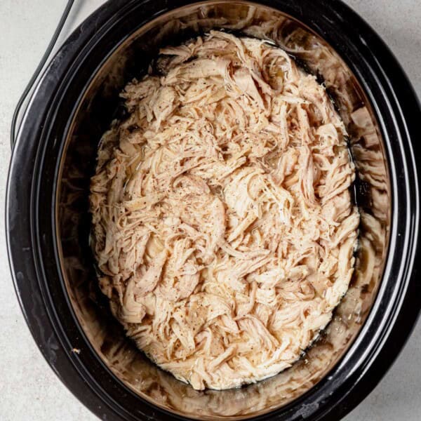 juicy shredded chicken in the slow cooker with salt and pepper on top.