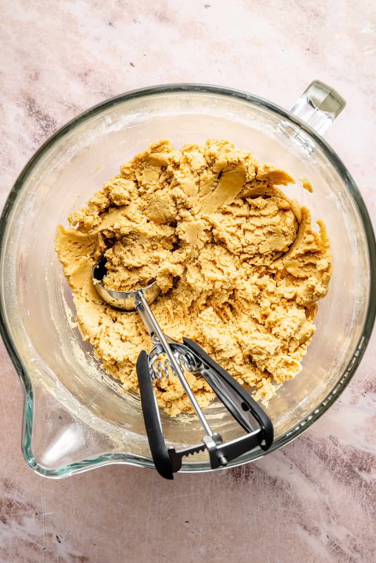 peanut butter cookie dough in a mixing bowl with a cookie scoop.