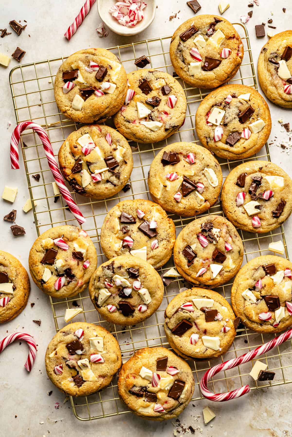 peppermint chocolate chip cookies on a cooling rack surrounded by chopped chocolate and candy canes.