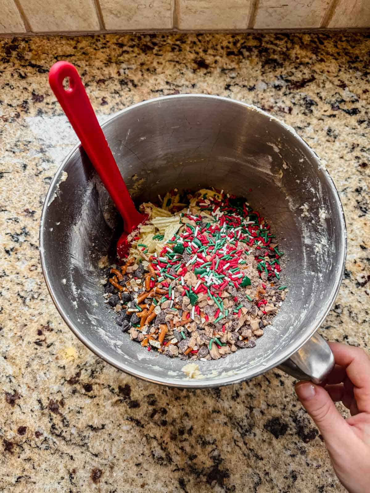 mixing christmas sprinkles, chocolate pretzels, and toffee into cookie dough.