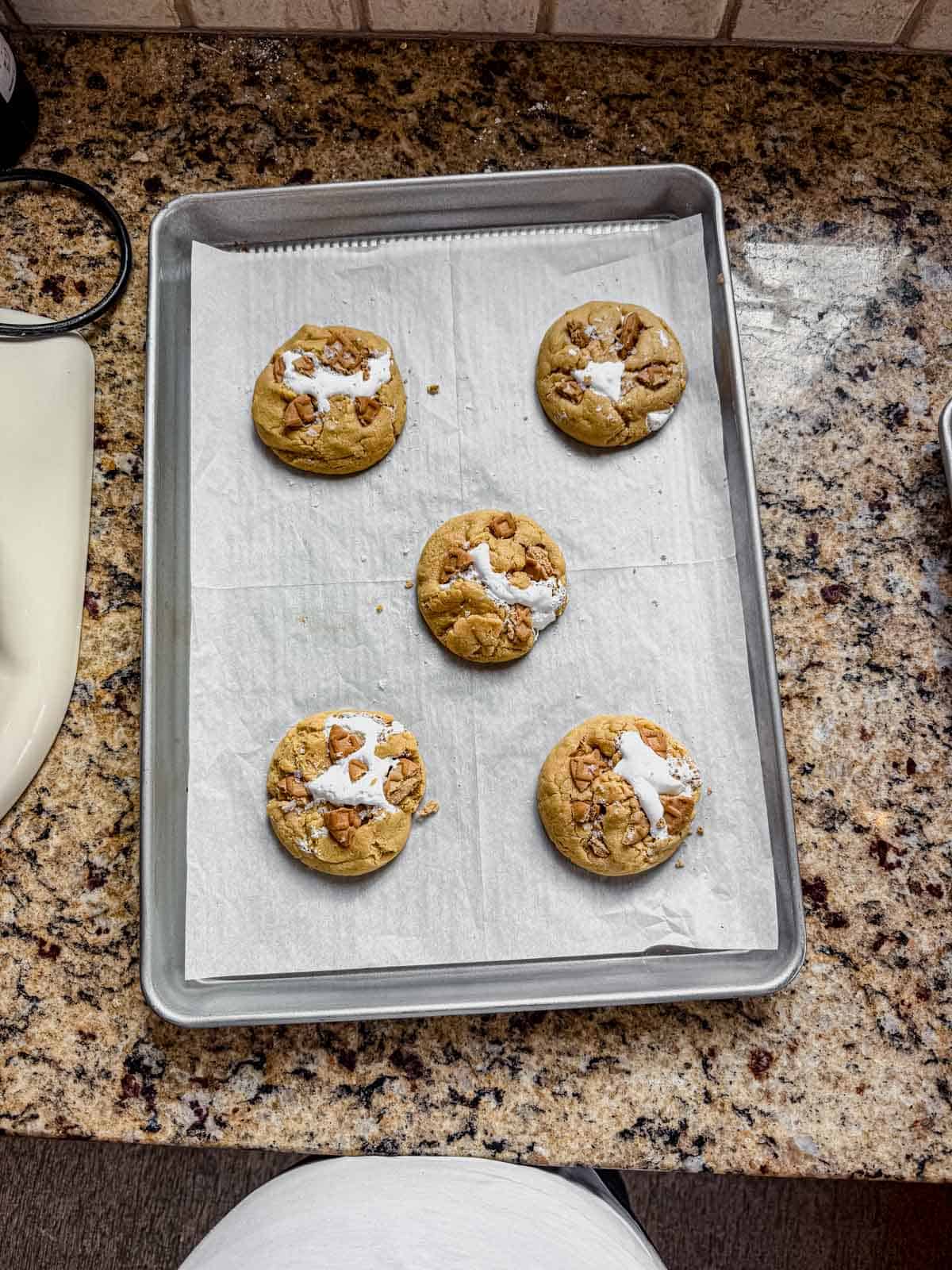 large pieces of broken nutter butters pressed onto the tops of the baked fluffernutters sitting on a parchment lined cookie sheet