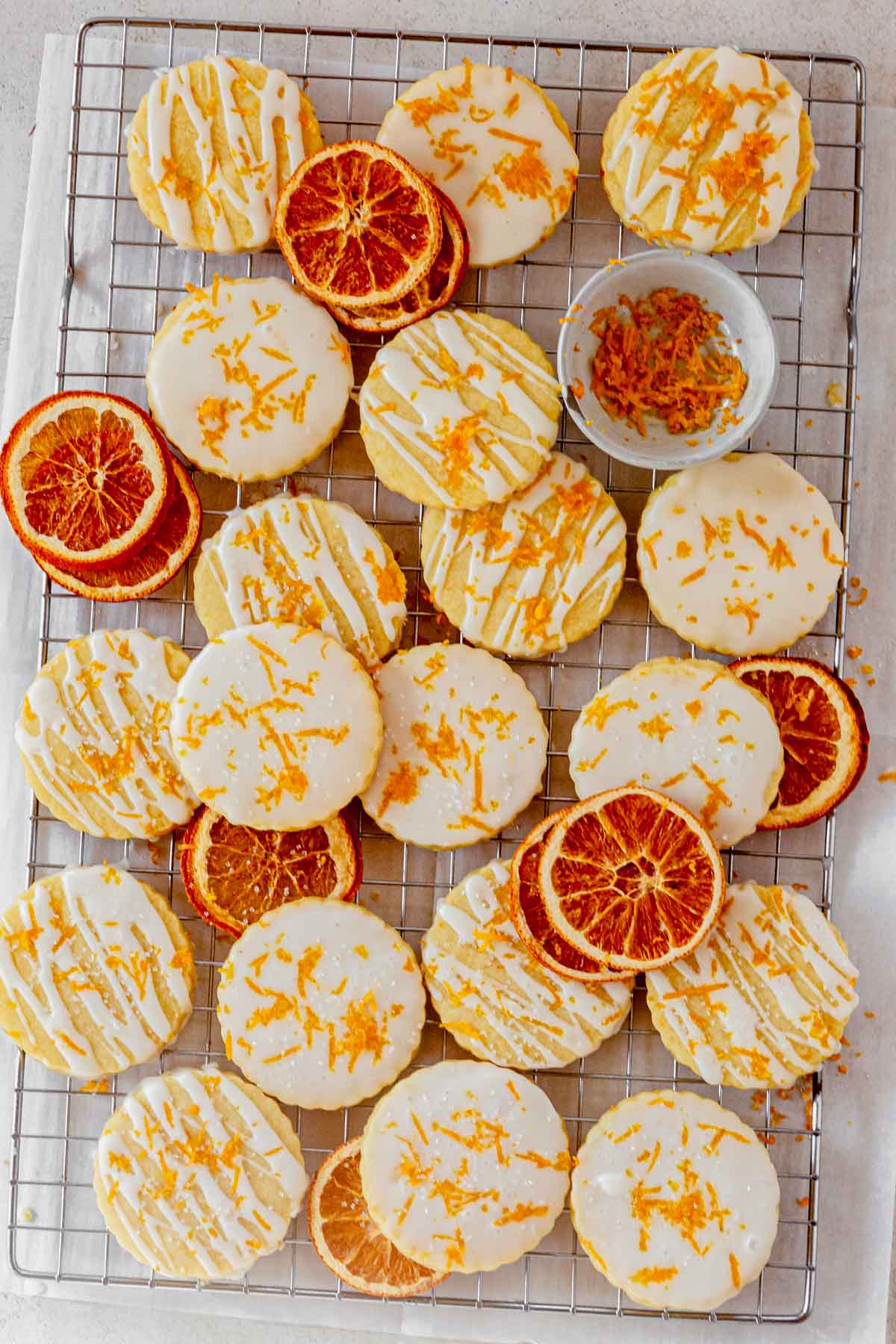 a batch of orange shortbread cookies on a cooling rack with slices of dried oranges.