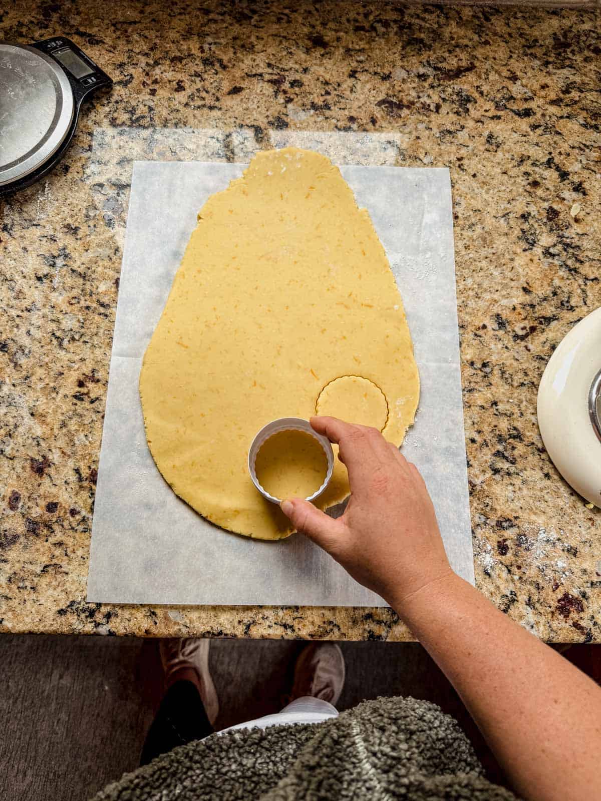 cutting round cookie shapes out of orange shortbread cookie dough.