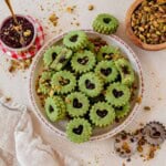 pistachio linzer cookies stacked on a Christmas plate on a counter with crushed pistachios