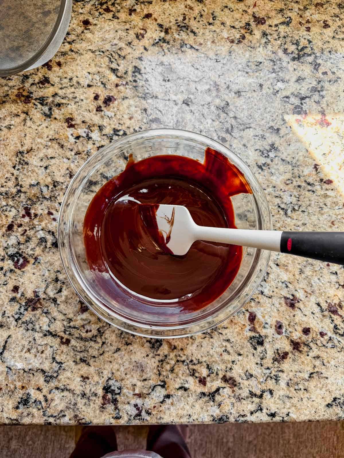 melted dark chocolate in a glass bowl with a white rubber spatula dipped into it.
