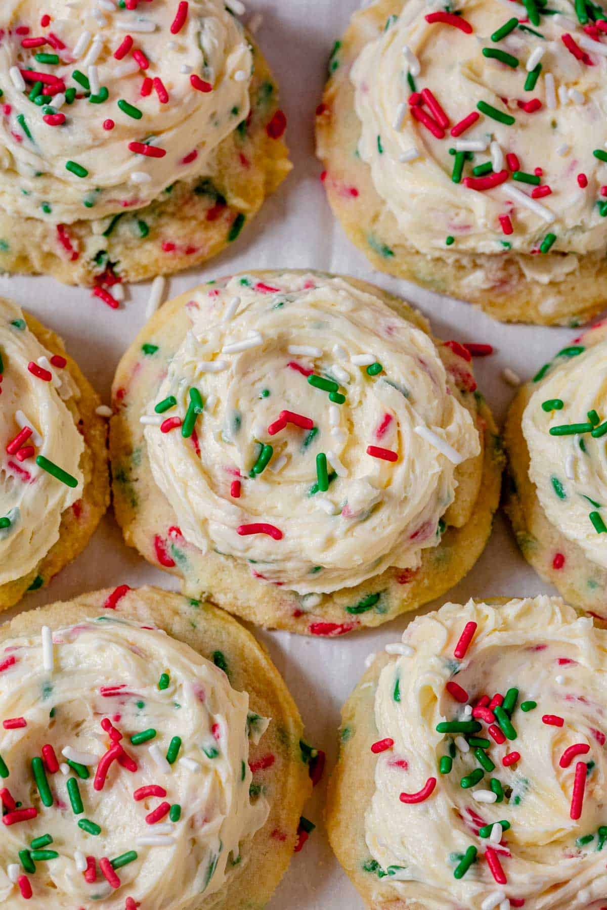 frosted christmas sugar cookies on a counter topped with holiday sprinkles.