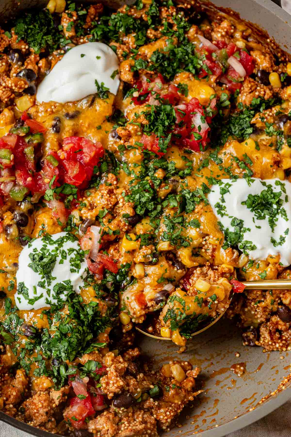 enchilada quinoa skillet topped with sour cream and cilantro with a spoon scooping a portion out.