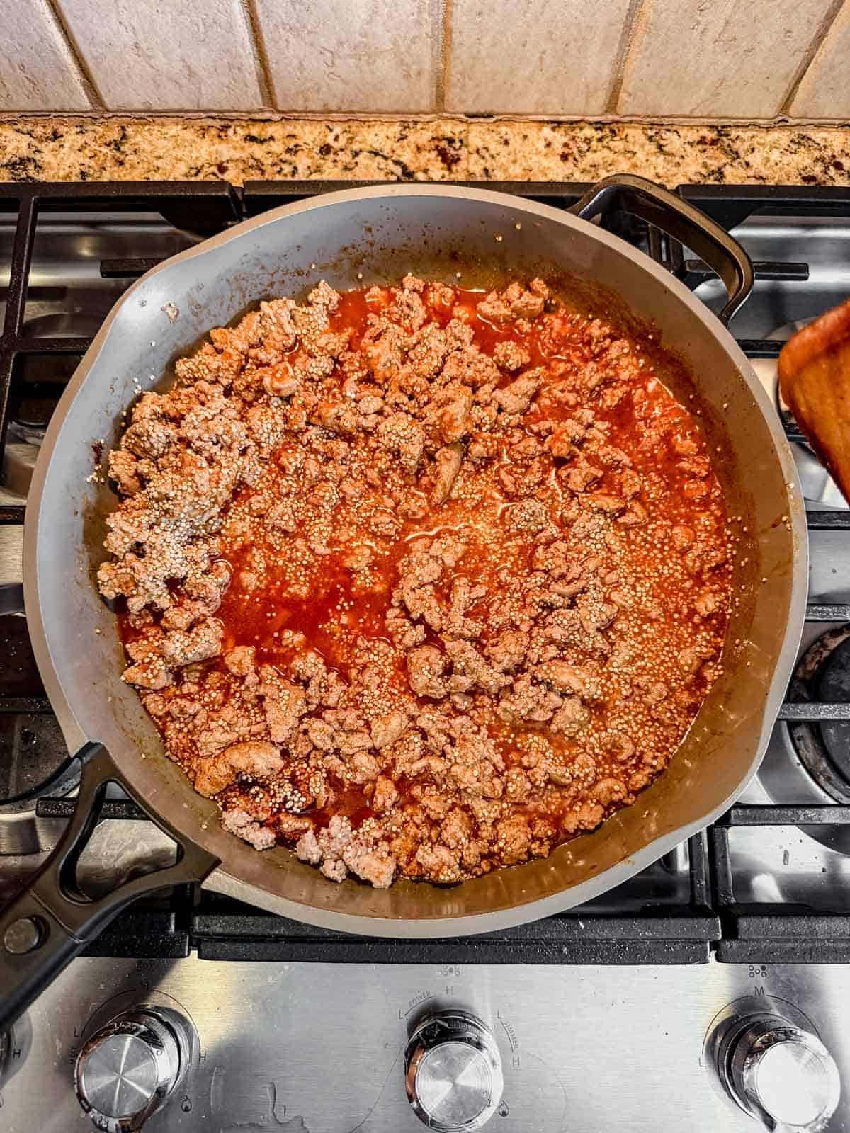 ground turkey, uncooked qunioa, broth, and enchilada sauce in a skillet.