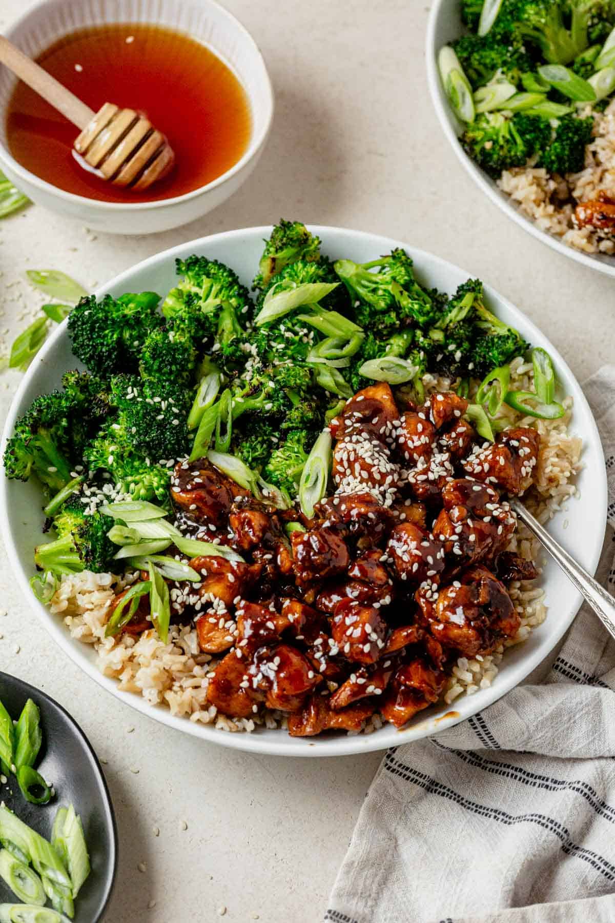honey garlic chicken and rice bowl topped with sesame seeds next to a bowl of honey.