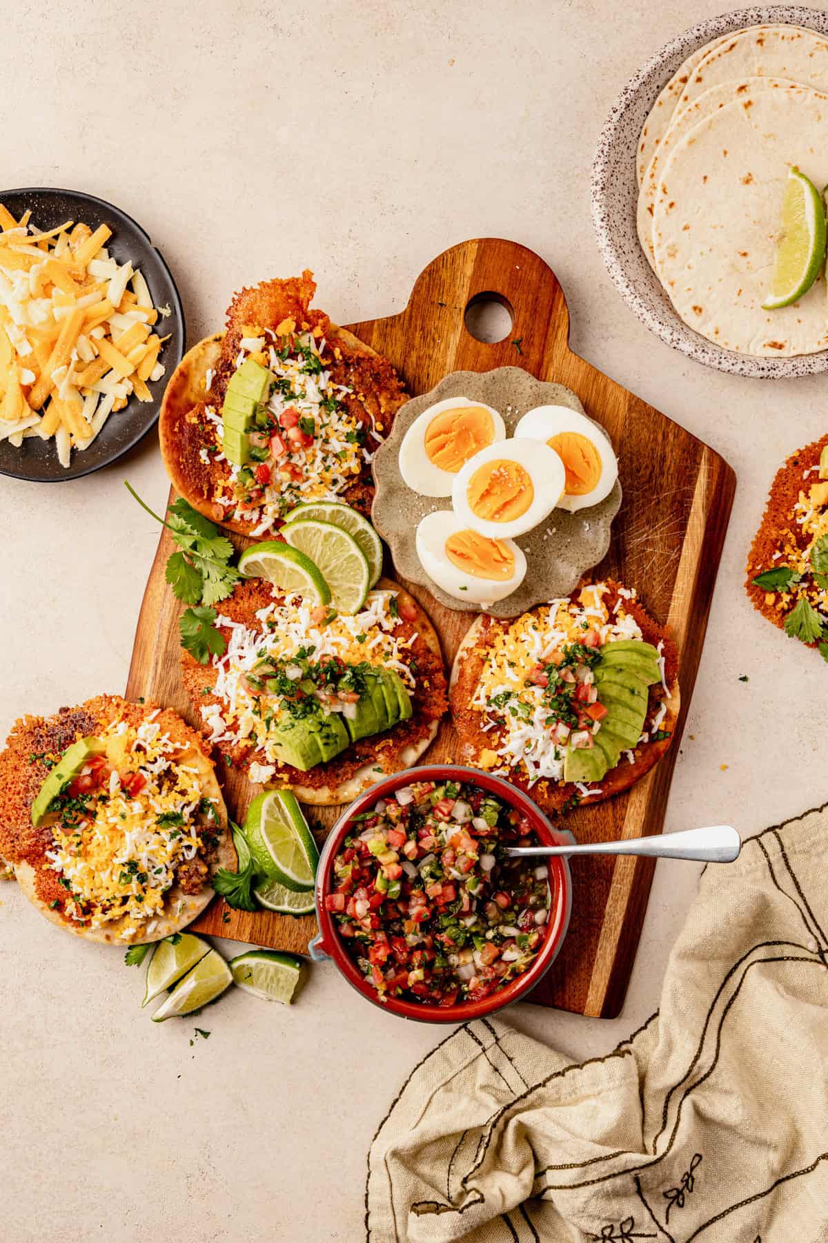5 breakfast smashed tacos on a cutting board with pico de gallo and hard boiled eggs.