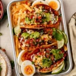 three breakfast smash tacos topped with avocado, pico de gallo, and lime.