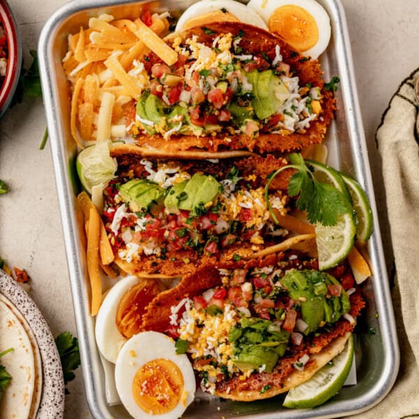 three breakfast smash tacos topped with avocado, pico de gallo, and lime.