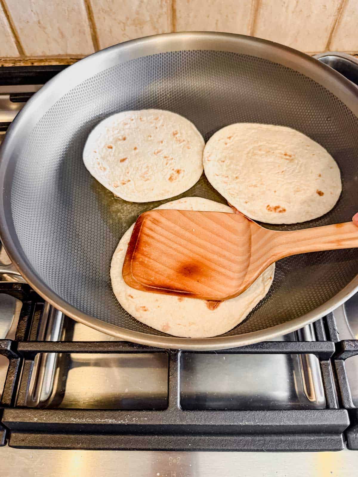 pressing a smashed taco onto a hot skillet with a wooden spatula.