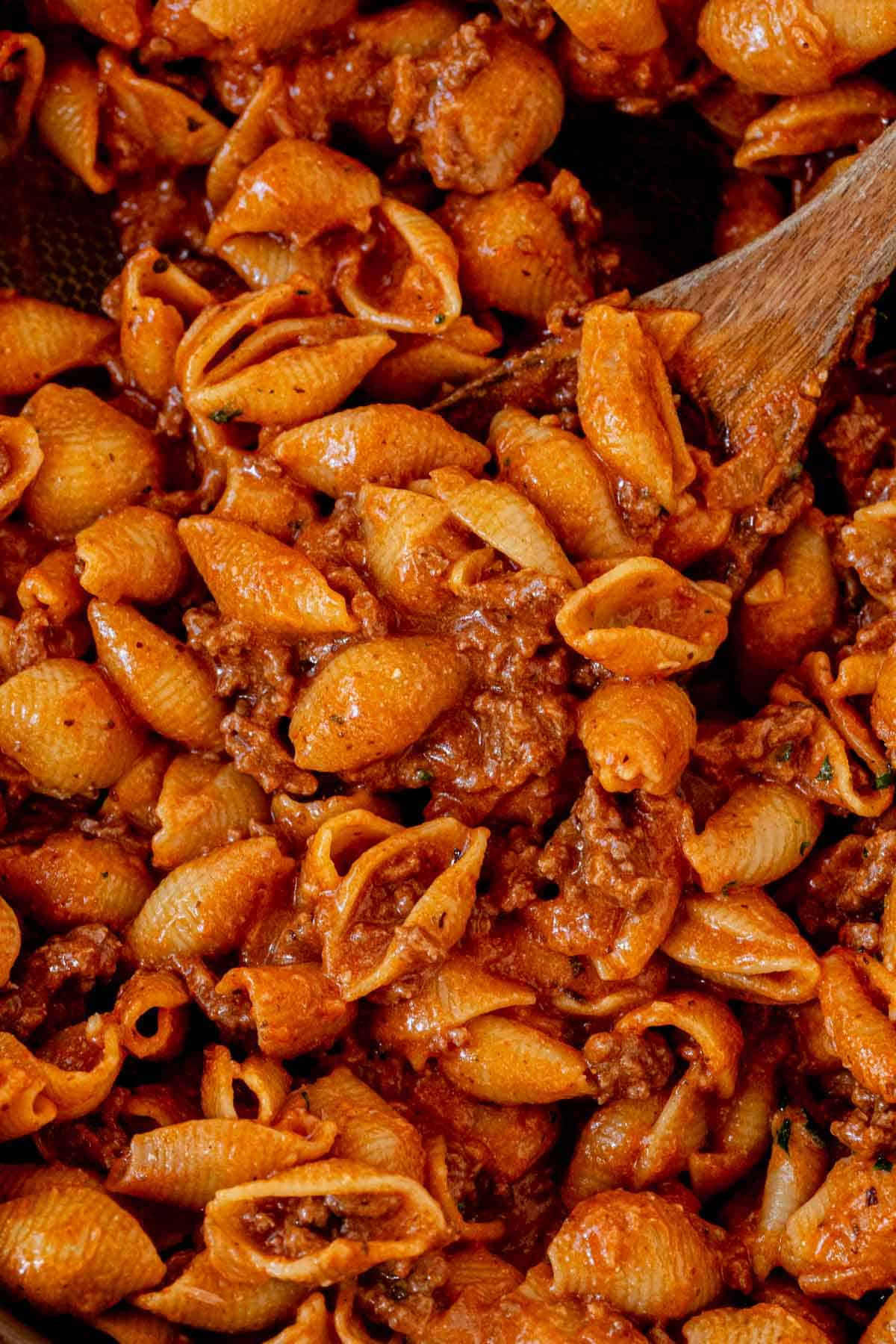a serving spoon scooping creamy beef and shells out of a skillet.
