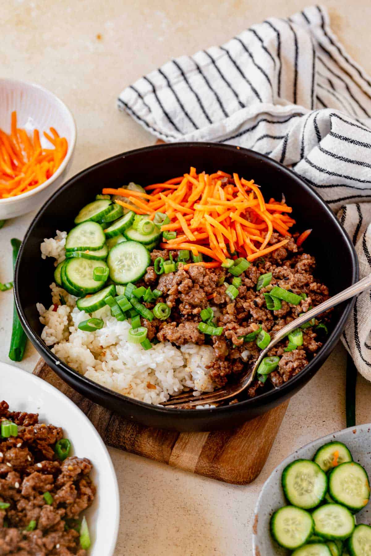 a fork scooping up rice, korean ground beef and veggies from a bowl.