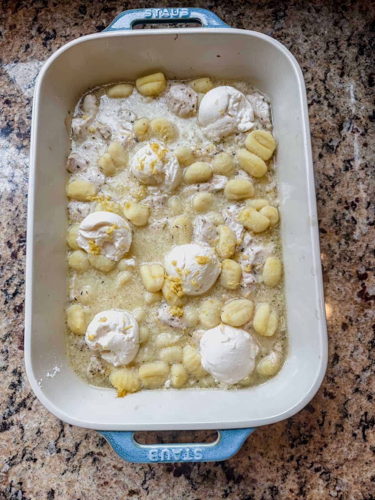 uncooked lemon chicken gnocchi topped with ricotta in a baking dish.