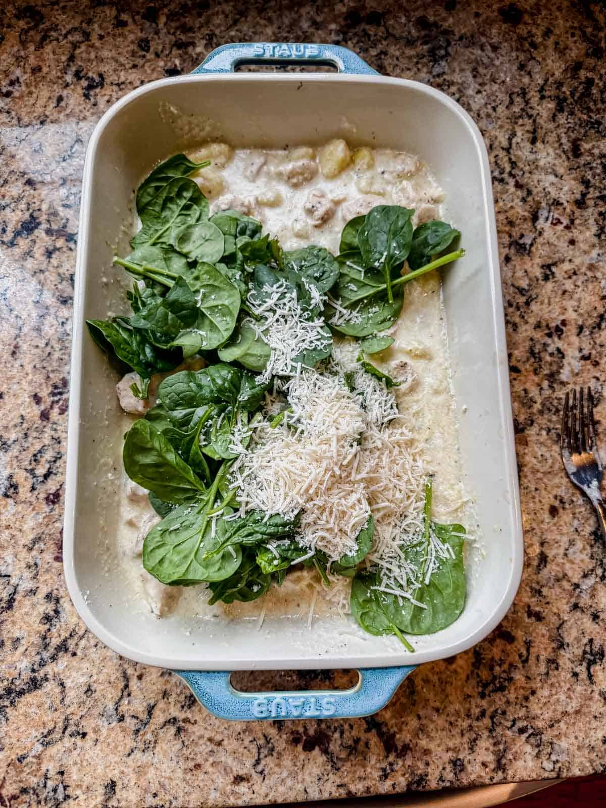 creamy lemon chicken gnocchi in a baking dish with fresh spinach and parmesan on top.
