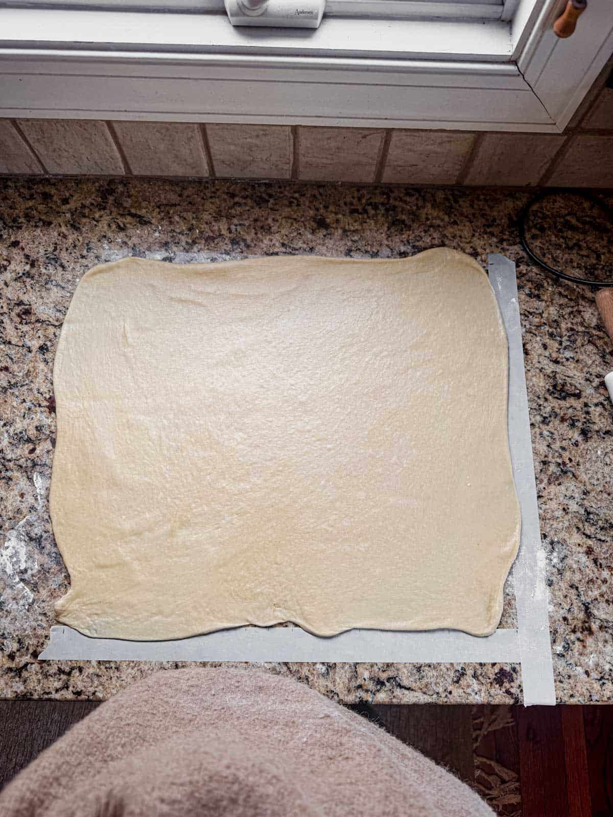 cinnamon roll dough rolled out into a rectangle on a counter.