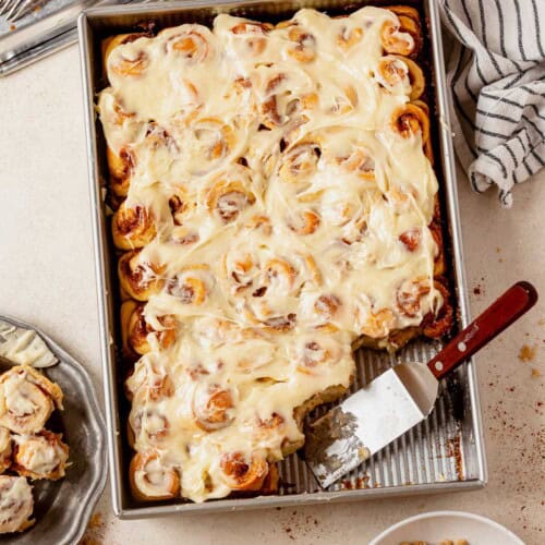 mini cinnamon rolls in a pan with a plate full of cinnamon rolls next to it.