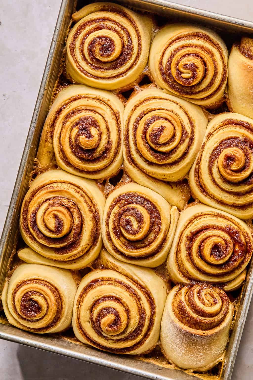 fluffy soft baked cinnamon rolls in a baking pan before frosting.
