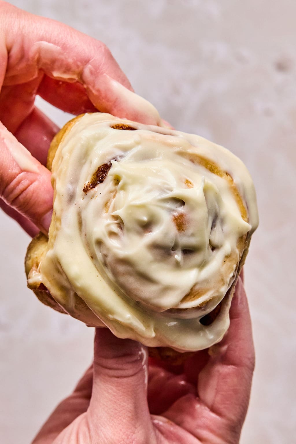 holding a super soft cinnamon roll with cream cheese frosting.