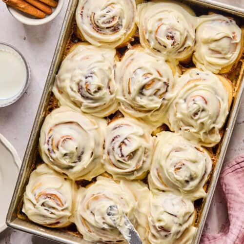 a baking pan full of super soft cinnamon rolls covered in cream cheese frosting.